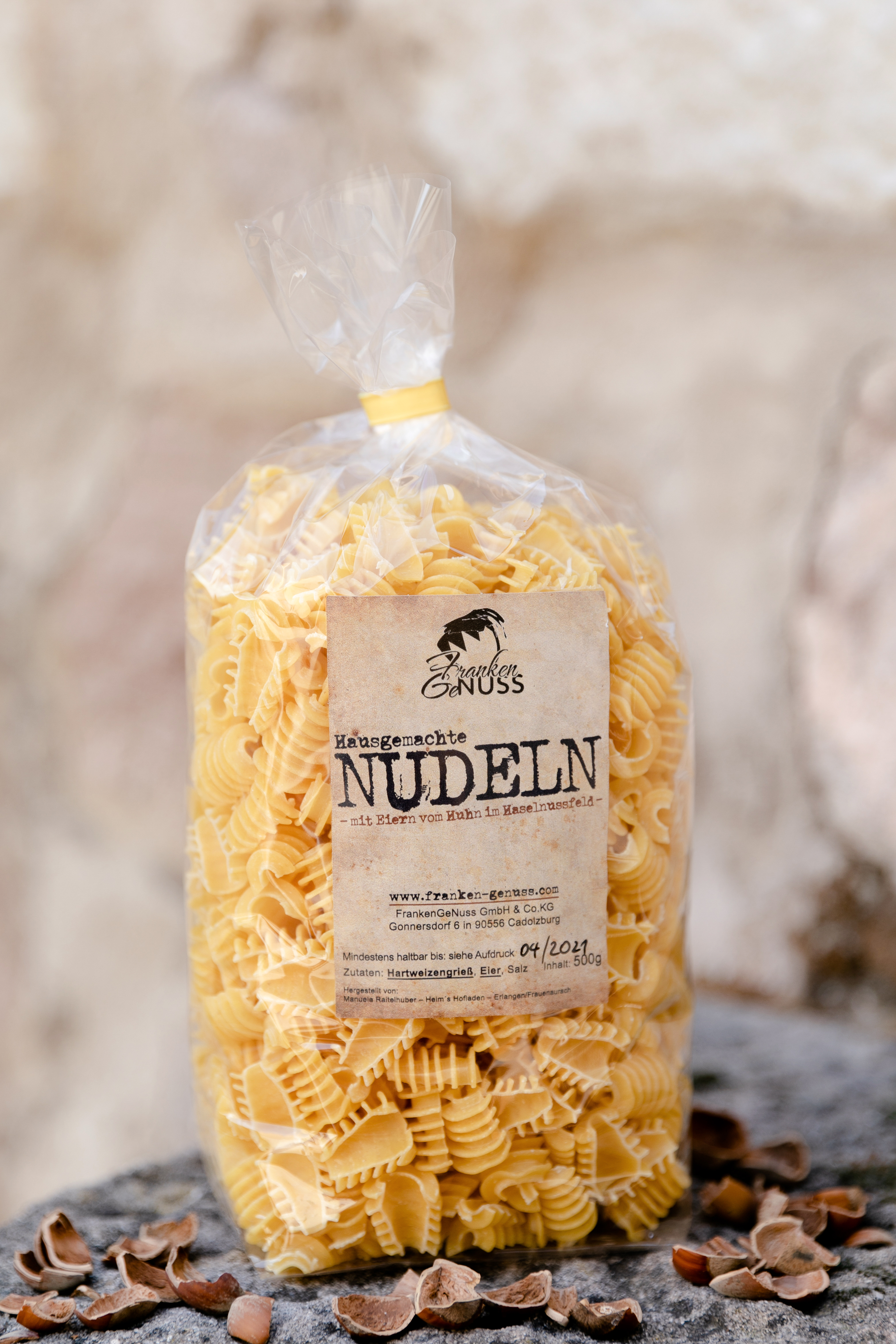 Eine gefüllte Verpackung mit gelben, gedrehten Nudeln steht auf einem steinigen Untergrund.