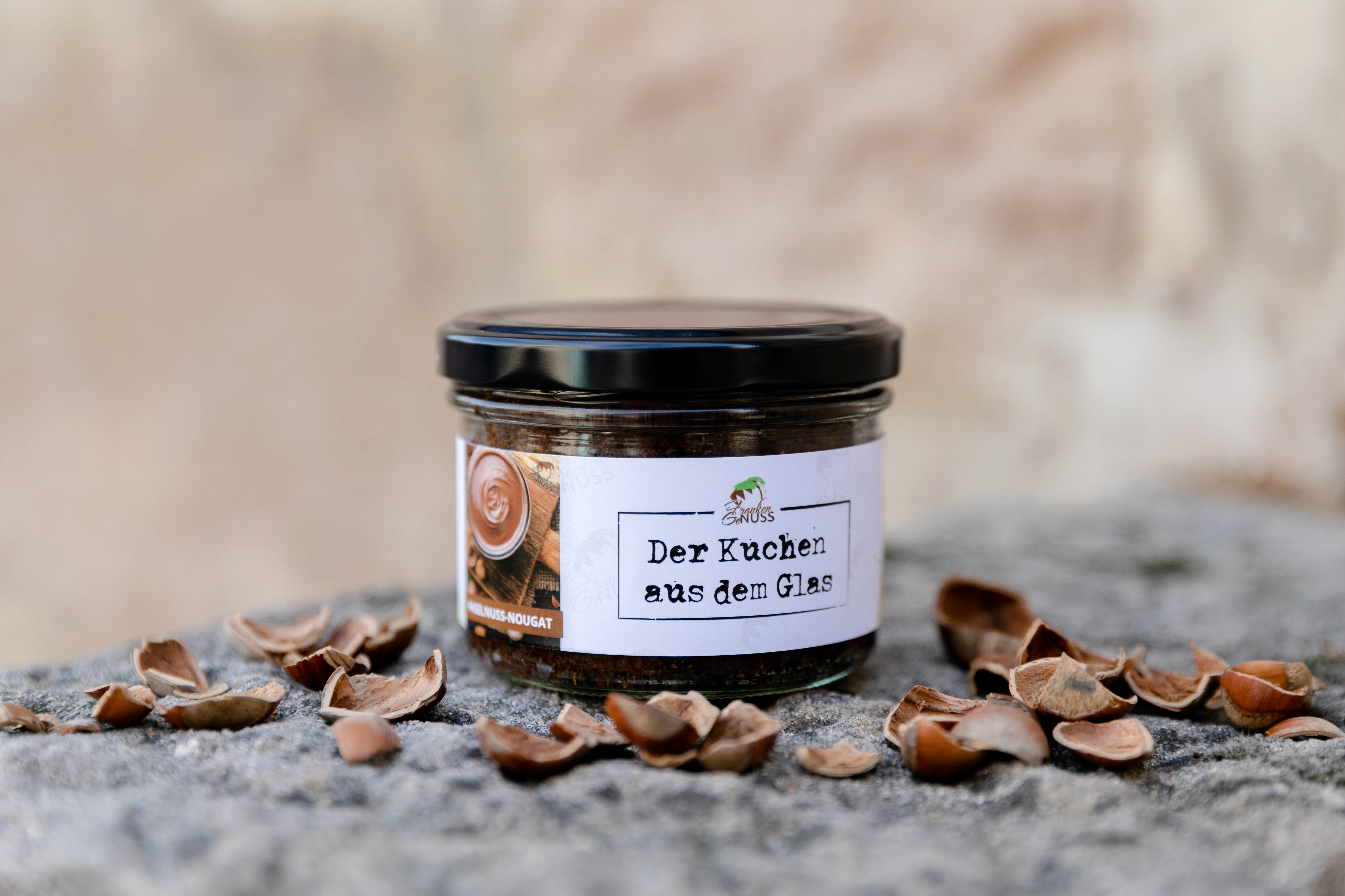 Ein Nougat-Kuchen aus dem Glas steht dekorativ auf Stein, umgeben von knackigen Haselnussschalen.