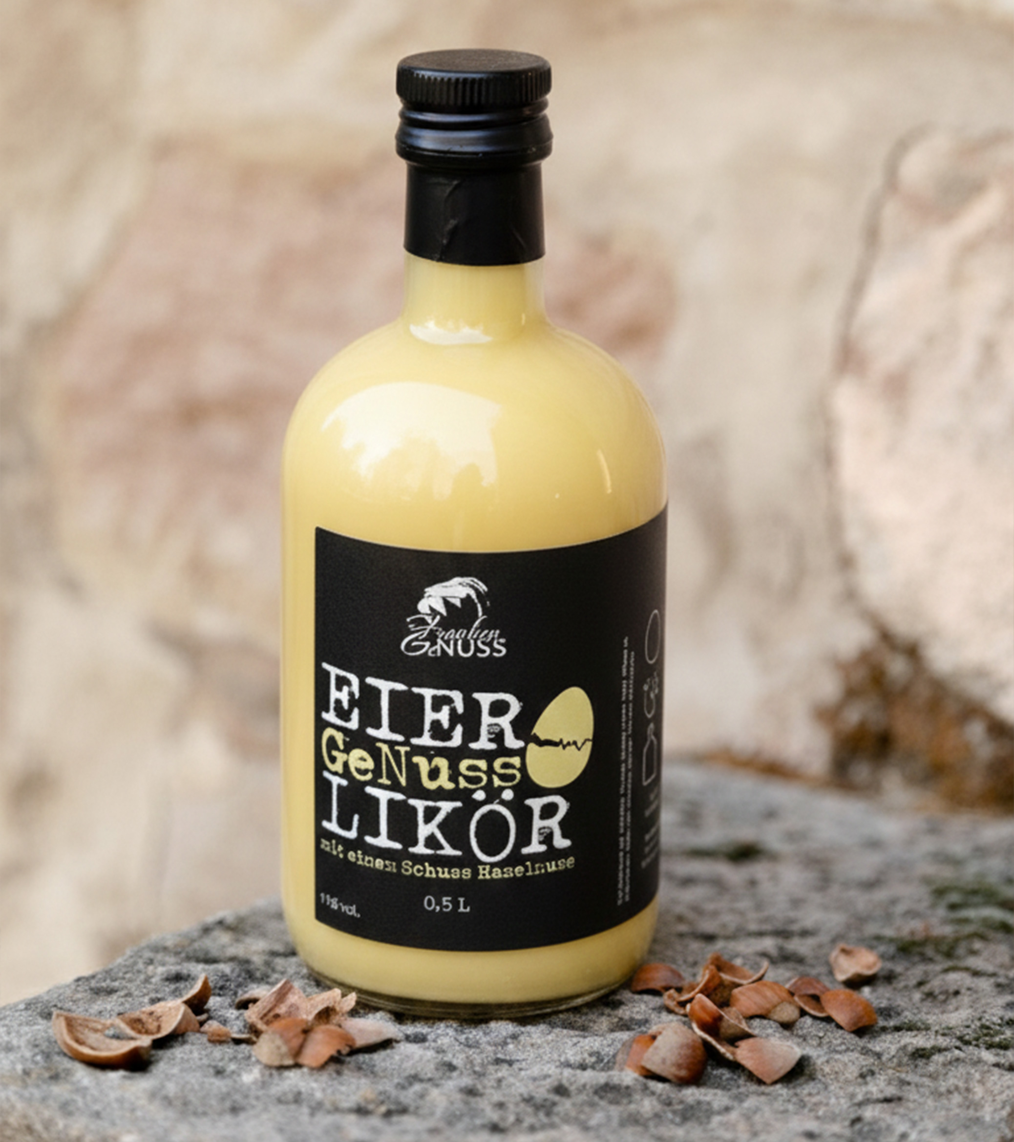 Eine Glasflasche mit cremig gelbem Eier-GeNuss-Likör steht auf Stein, umgeben von knackigen Haselnussschalen. Eine Glasflasche mit cremig gelbem Eier-GeNuss-Likör steht auf Stein, umgeben von knackigen Haselnussschalen.