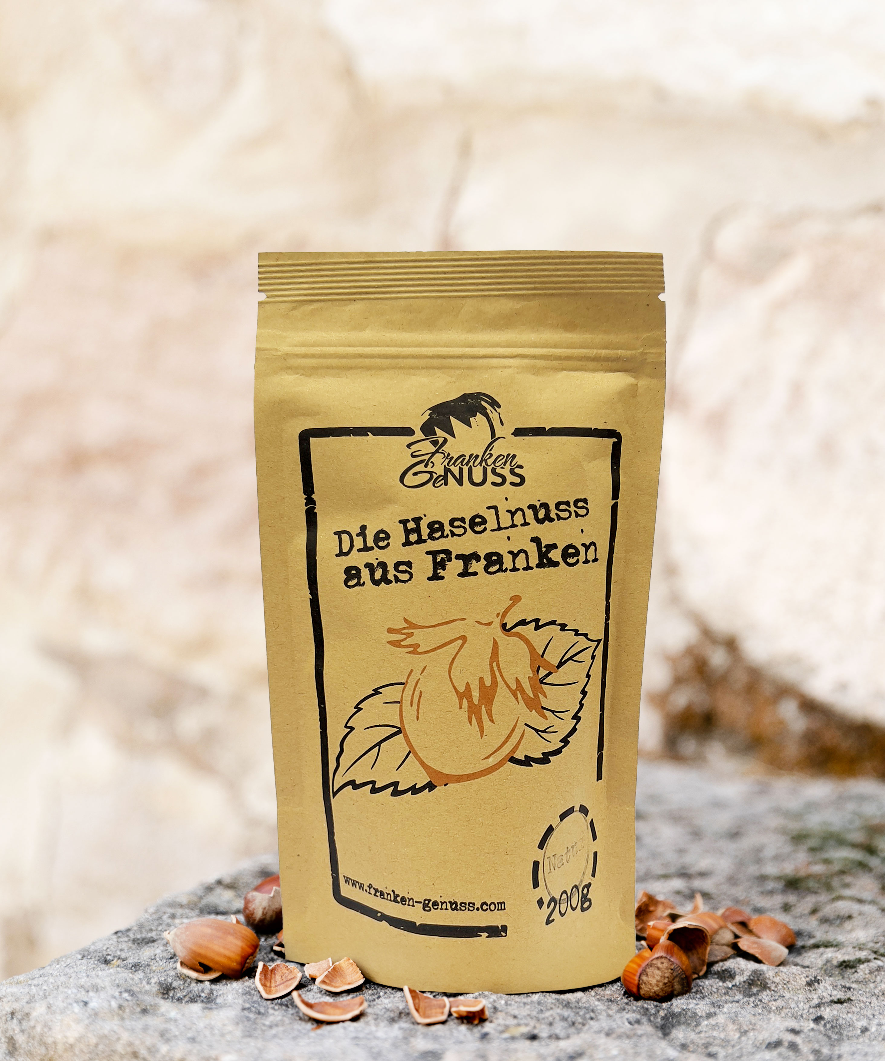 Eine stehende Verpackung mit Haselnuss-Illustration steht auf einem Stein inmitten von einigen Haselnüssen.