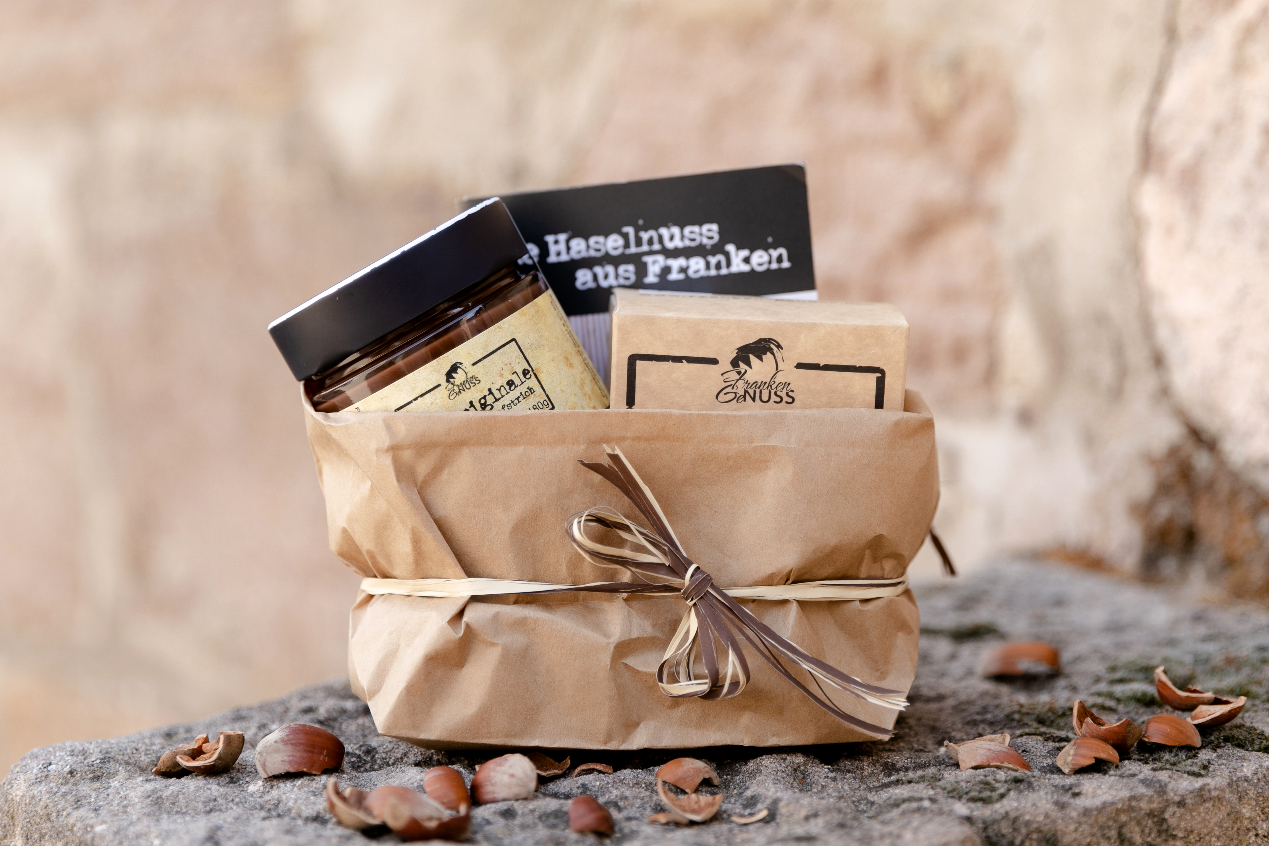 Ein liebevoll in Packpapier verpacktes GeNuss-Geschenk mit feinem Nougat und Cantuccini, umgeben von Haselnussschalen.