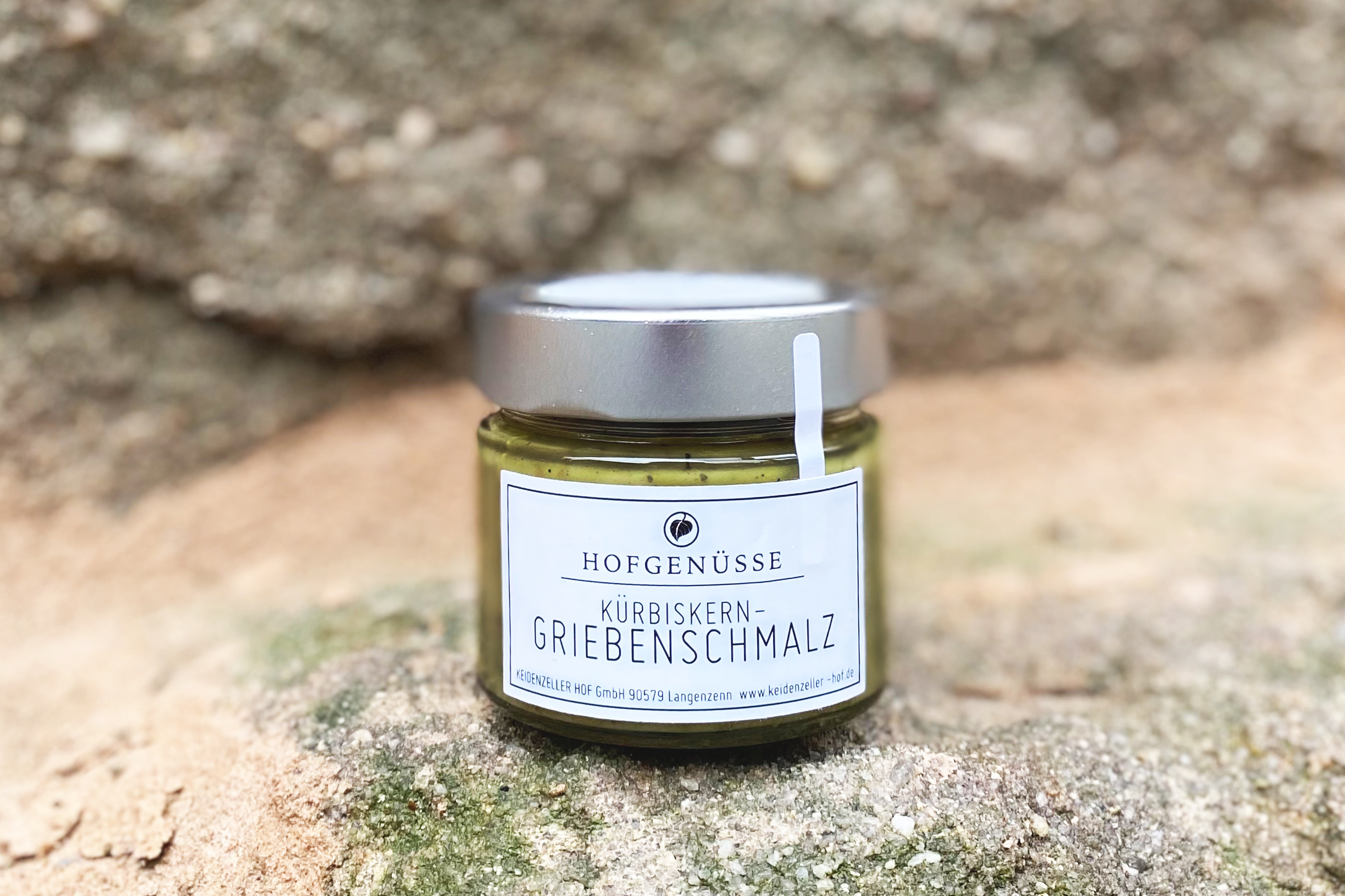 Ein kleines Glas mit cremigem Kürbis-Griebenschmalz steht auf einem natürlichen, felsigen Untergrund.