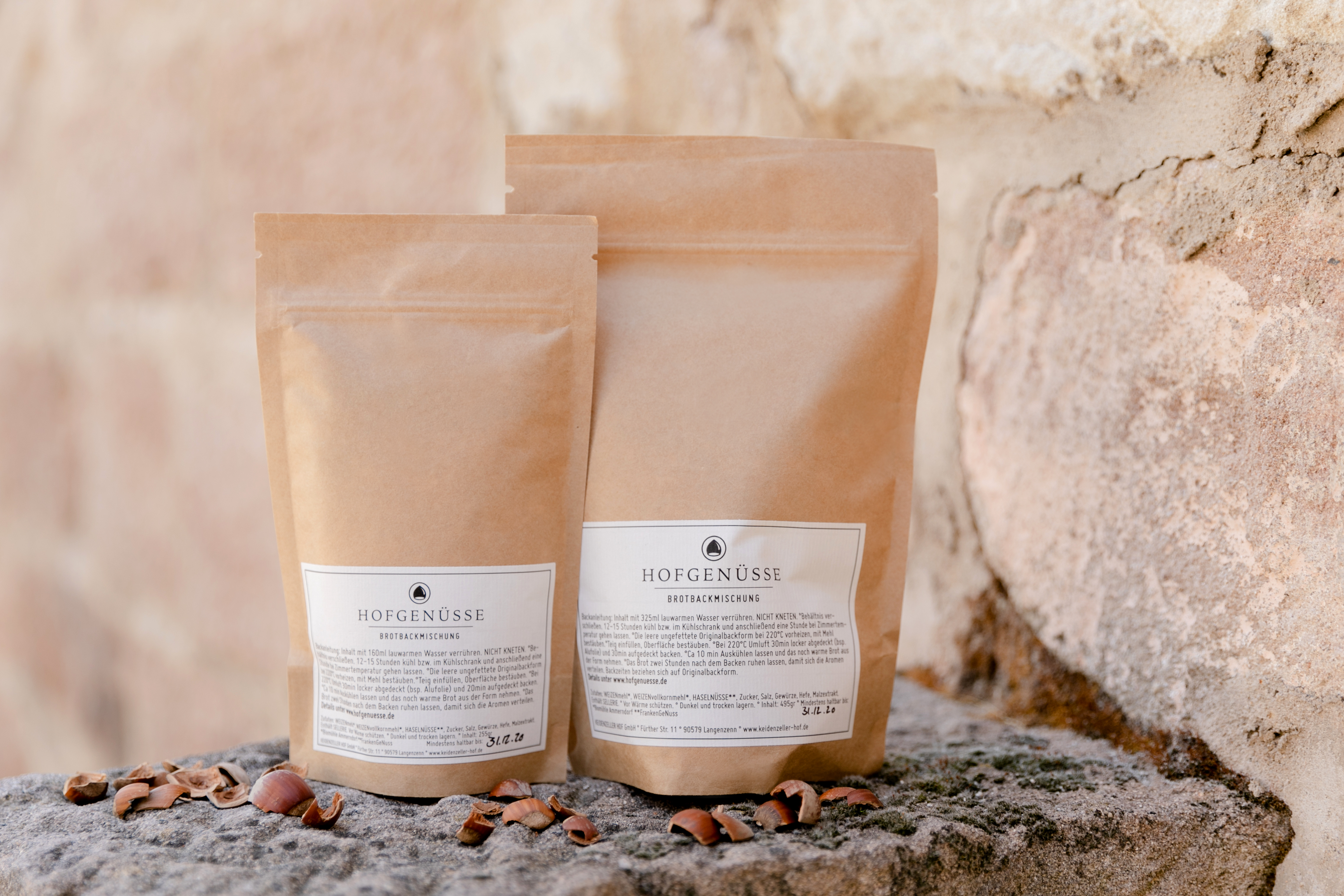 Zwei naturbraune Beutel der Brotbackmischung Gewürzbrot mit Haselnüssen liegen dekorativ auf einer rustikalen Steinmauer. Zwei naturbraune Beutel der Brotbackmischung Gewürzbrot mit Haselnüssen liegen dekorativ auf einer rustikalen Steinmauer.
