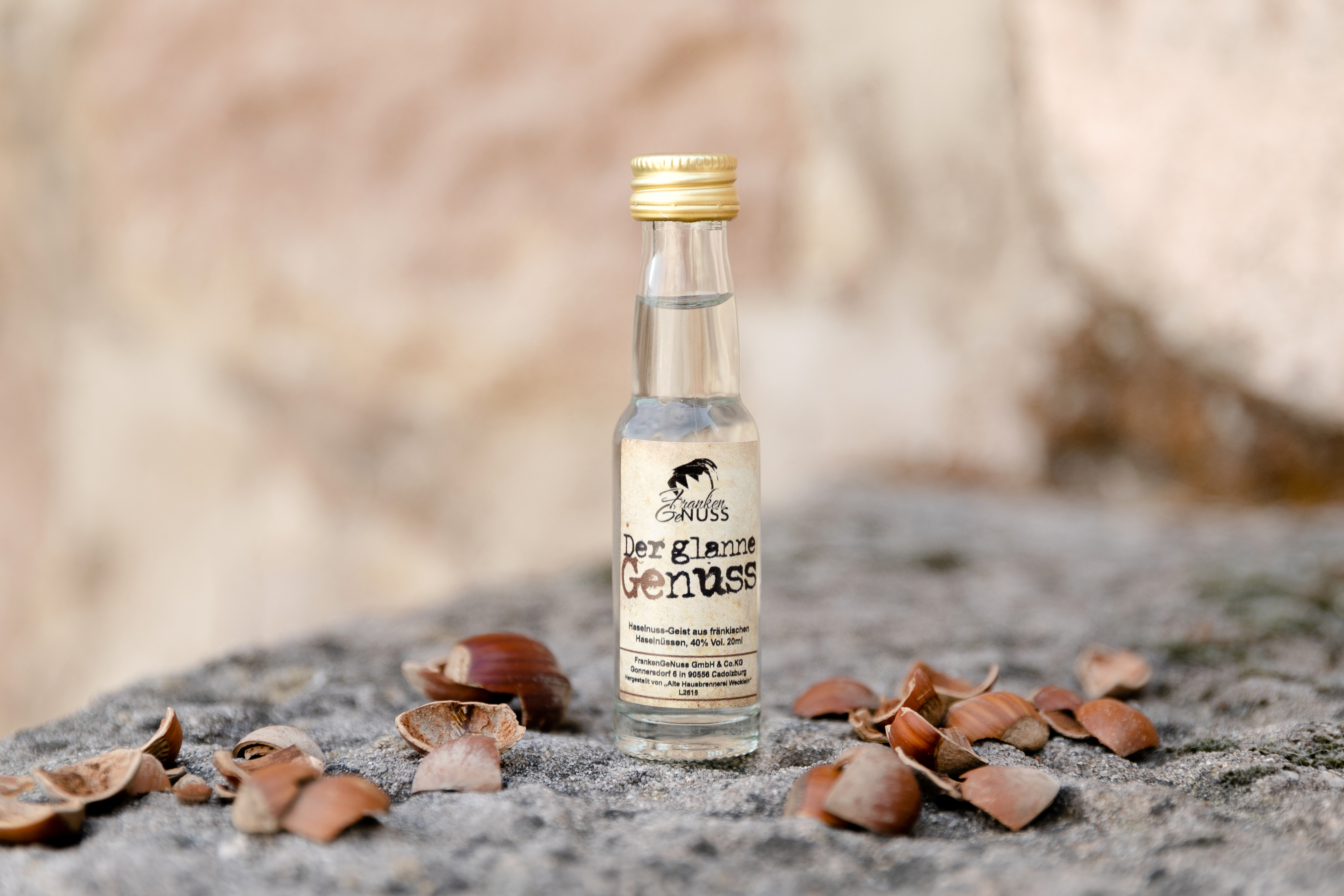 Eine kleine Flasche Fränkischer Haselnuss - Spirituose steht umgeben von knackigen Haselnussschalen auf einem rustikalen Stein. Eine kleine Flasche Fränkischer Haselnuss - Spirituose steht umgeben von knackigen Haselnussschalen auf einem rustikalen Stein.