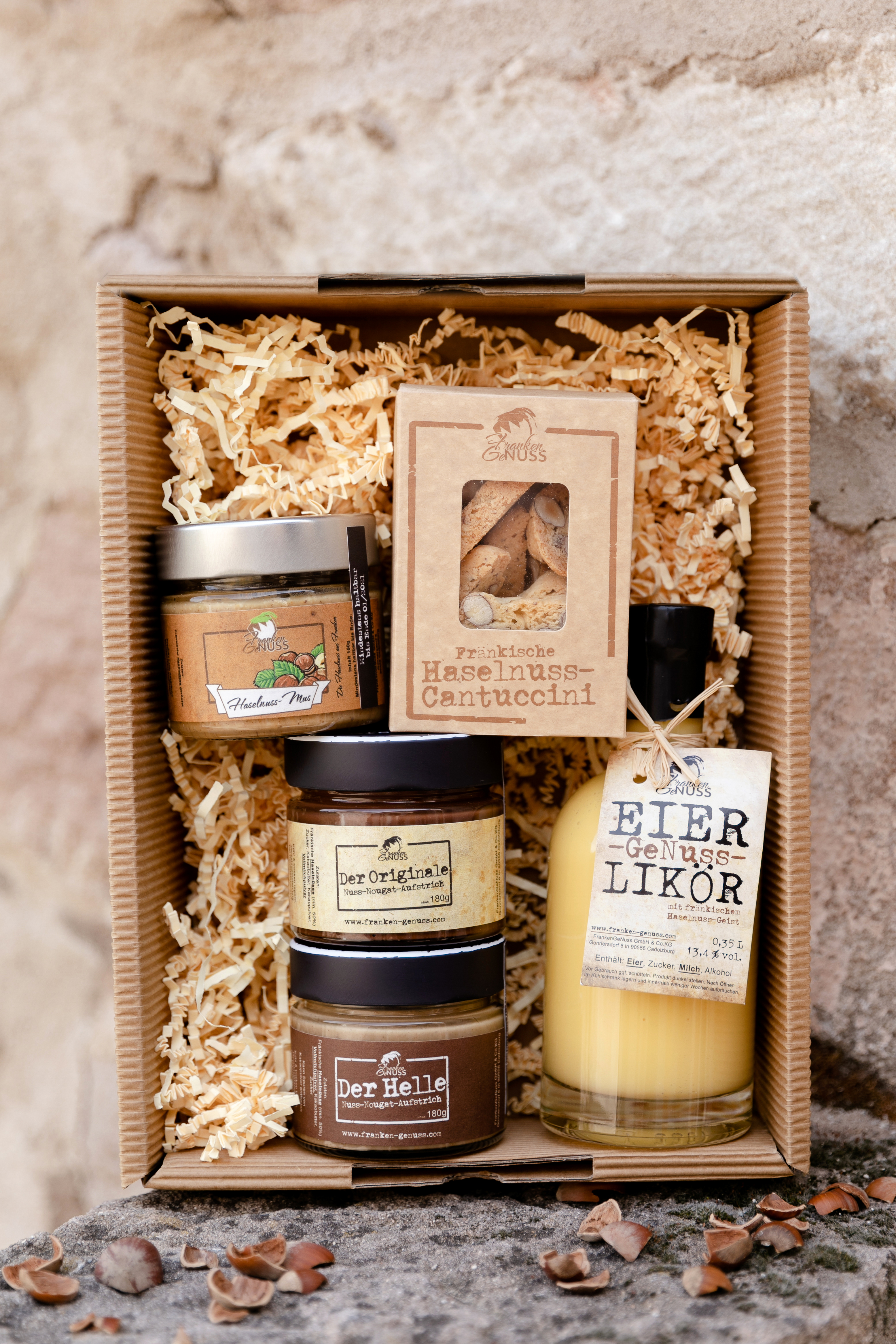 Eine prall gefüllte Geschenkbox „GeNuss-Vielfalt“ mit verschiedenen feinen Haselnussprodukten und Likör auf Holzwolle.