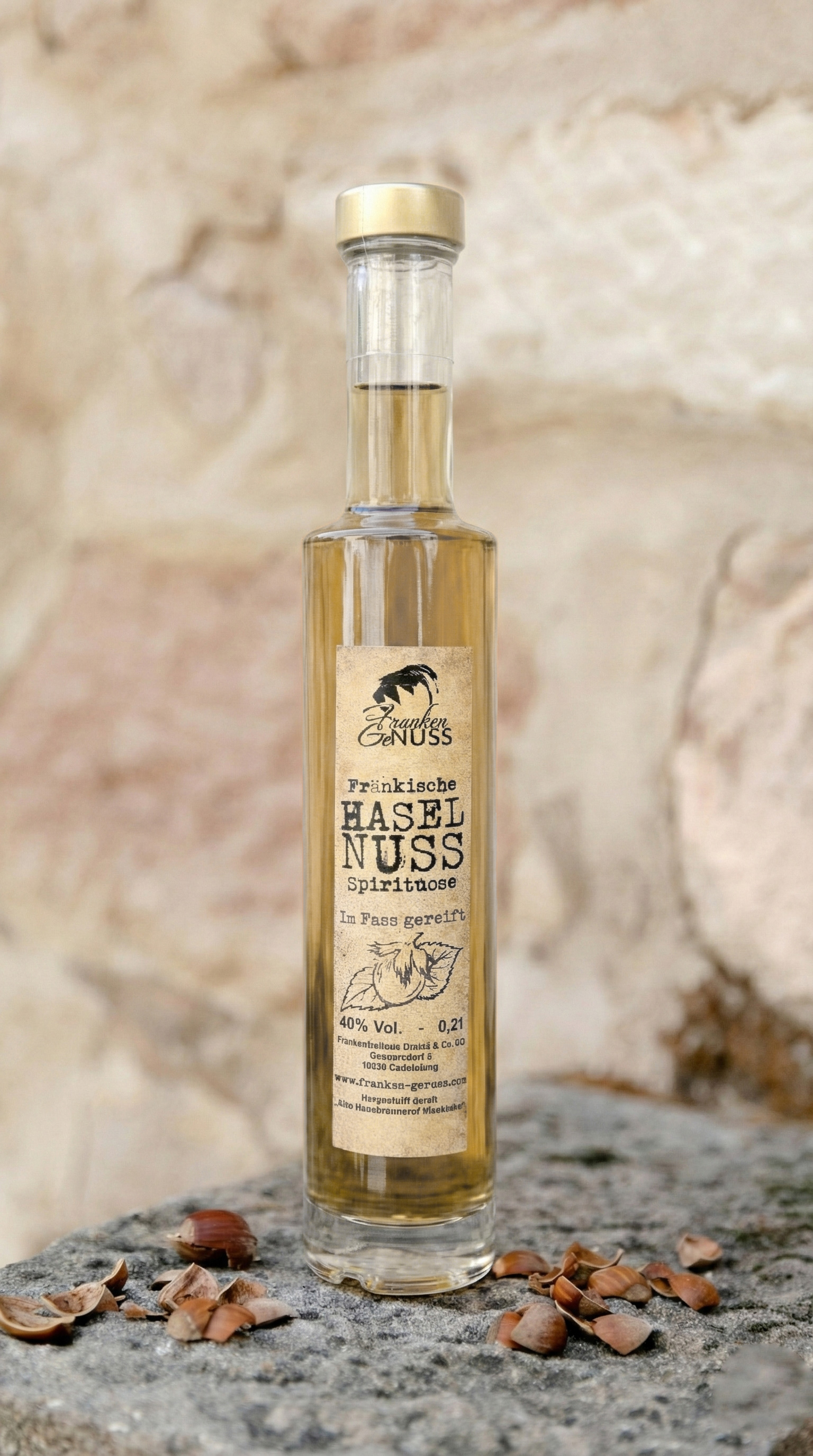 Eine schmale Flasche mit goldener Spirituose steht auf einem Stein vor einer Wand. Eine schmale Flasche mit goldener Spirituose steht auf einem Stein vor einer Wand.