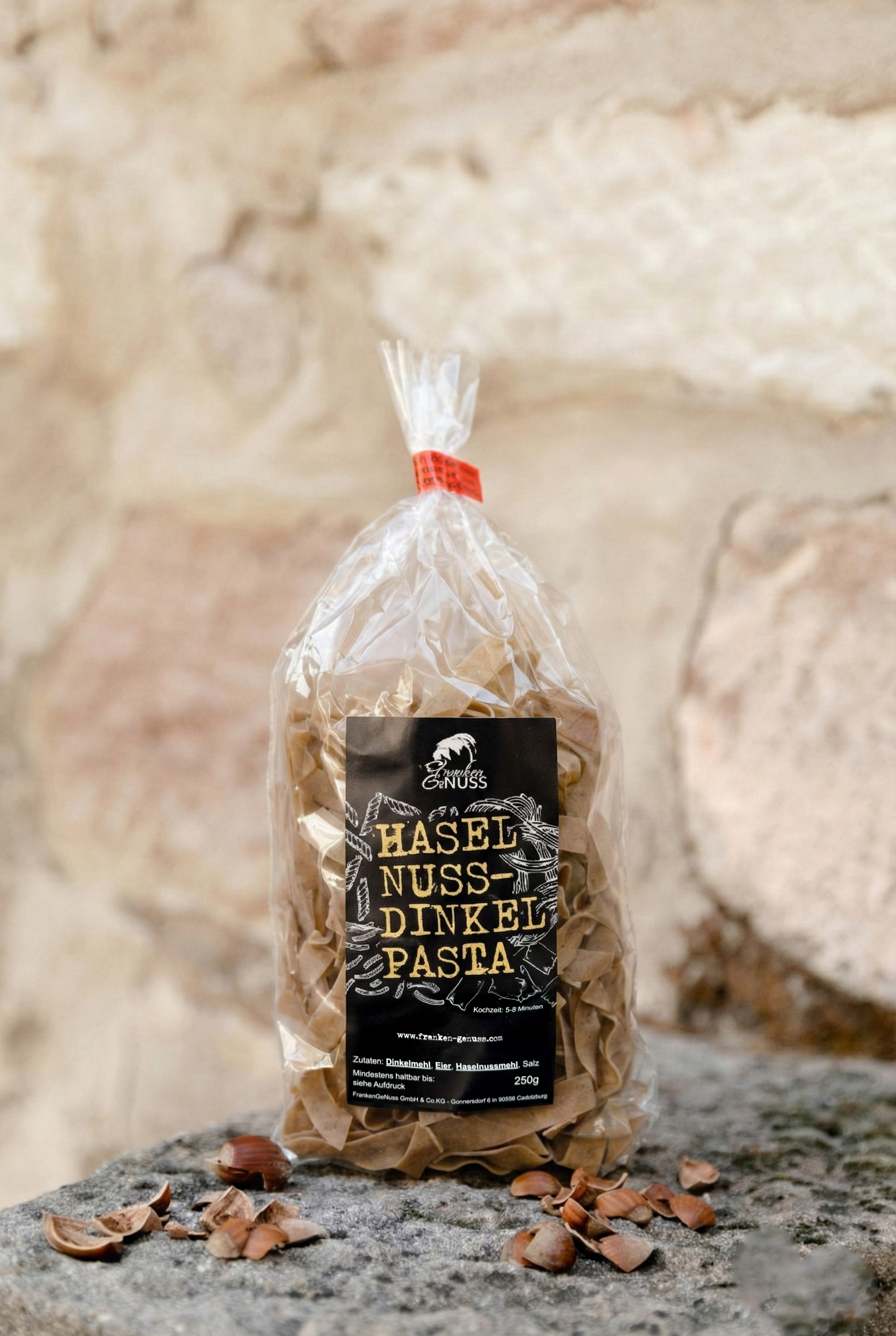 Eine gefüllte Verpackung mit braunen Nudeln steht auf einem Stein vor einer rustikalen Wand.