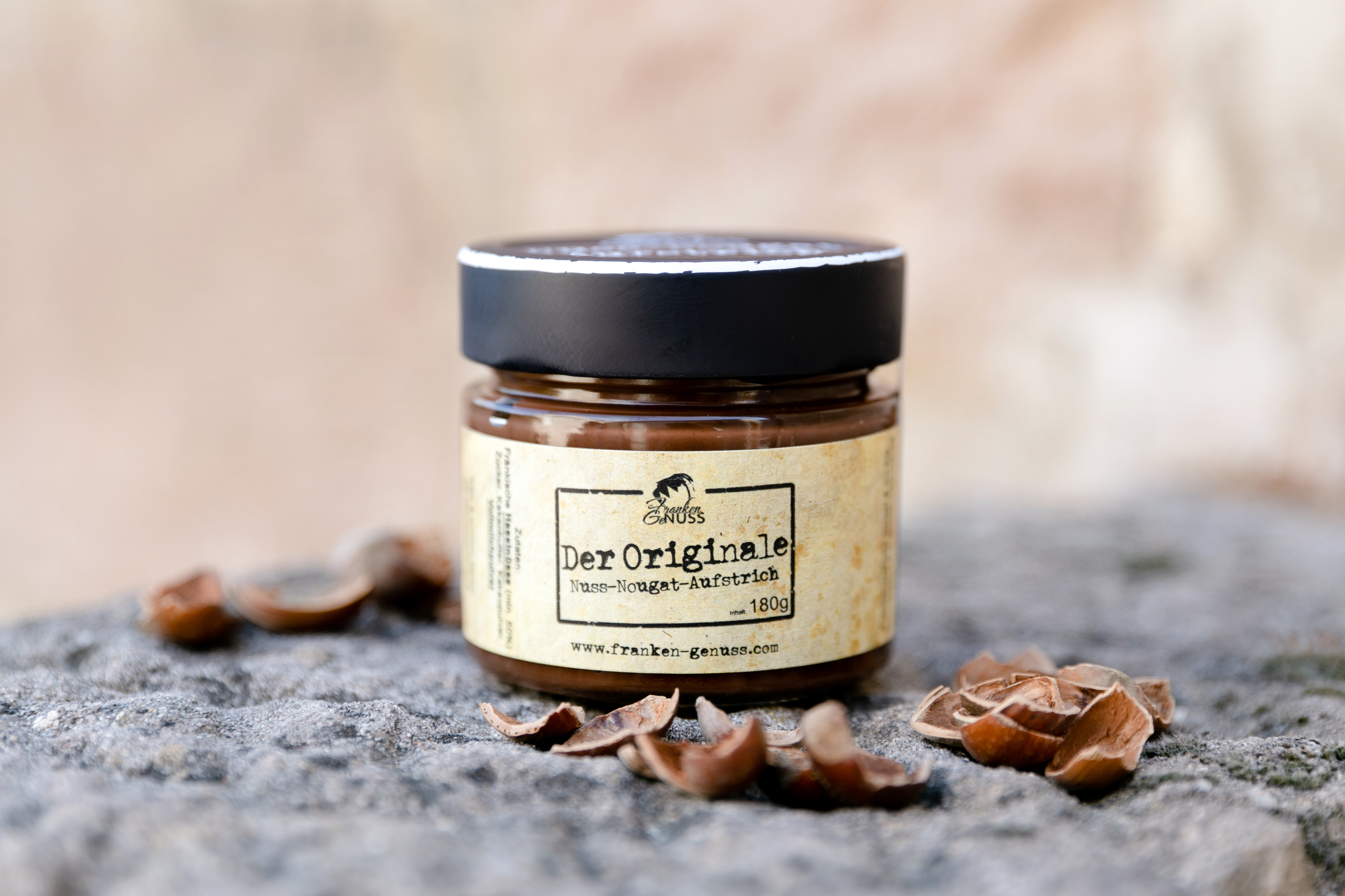 Cremiger Haselnuss-Nougat-Aufstrich in einem Glas, appetitlich umgeben von Haselnussschalen auf einem steinernen Untergrund. Cremiger Haselnuss-Nougat-Aufstrich in einem Glas, appetitlich umgeben von Haselnussschalen auf einem steinernen Untergrund.