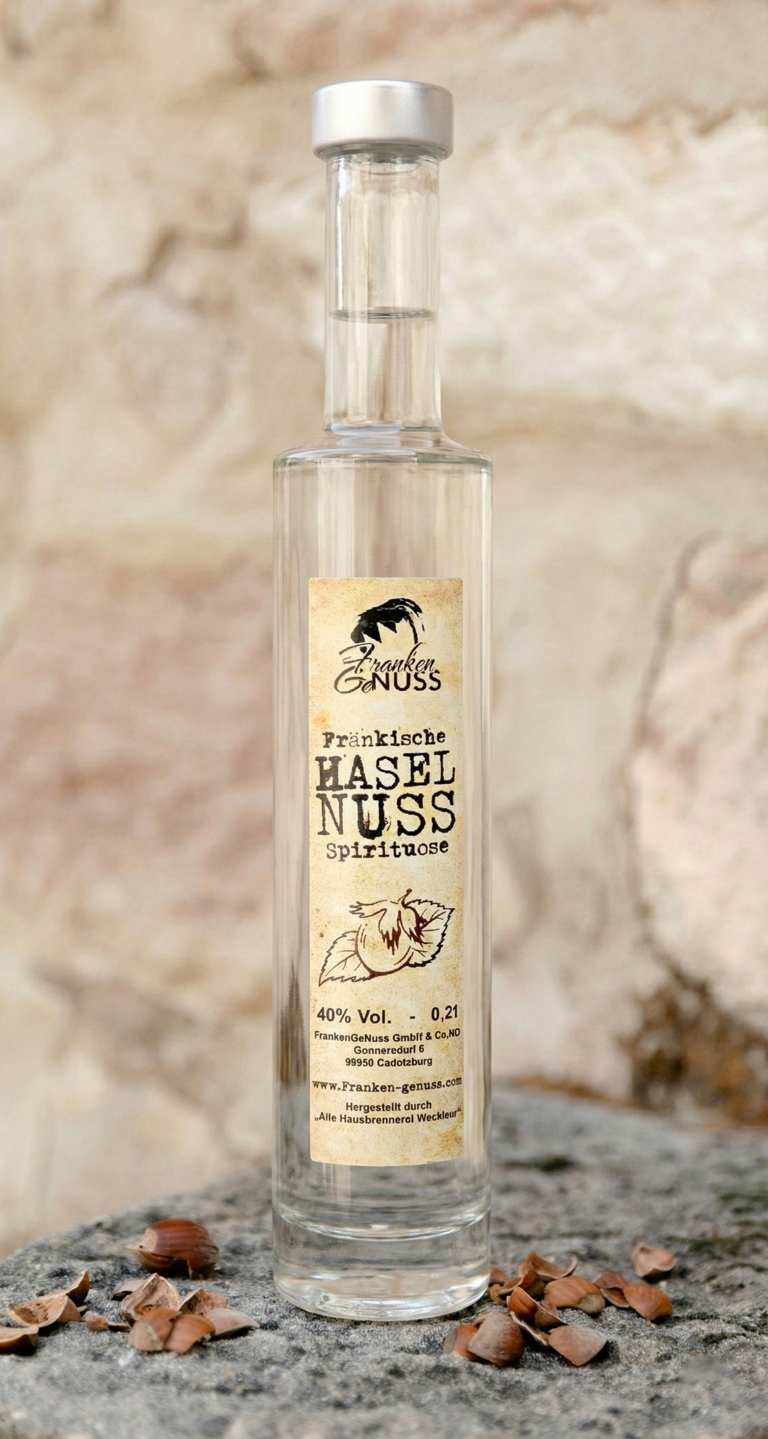 Eine schlanke Flasche mit klarer Spirituose steht auf einer steinernen Oberfläche umgeben von Nussschalen. Eine schlanke Flasche mit klarer Spirituose steht auf einer steinernen Oberfläche umgeben von Nussschalen.