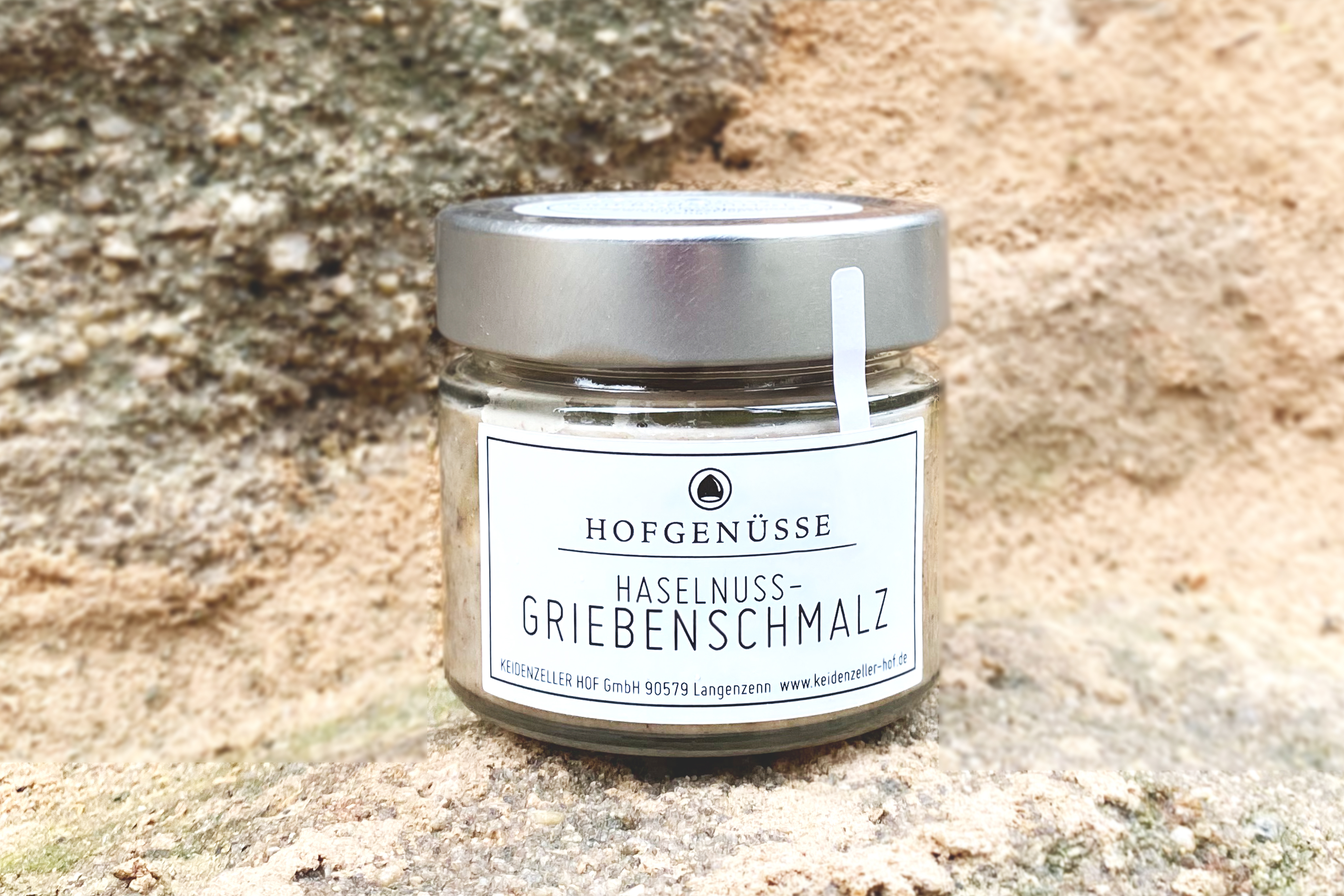 Ein Glas Haselnuss-Griebenschmalz steht auf einem rustikalen Untergrund aus hellem Stein.